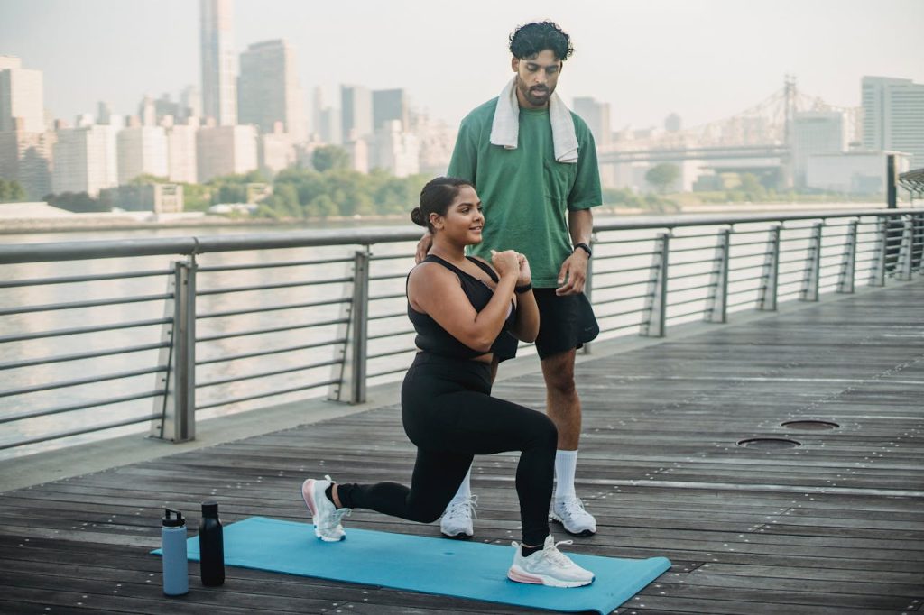 man-in-green-shirt-and-black-shorts-doing-push-up-5037398 Woman performing lunges on a boardwalk with a trainer by the river view.
