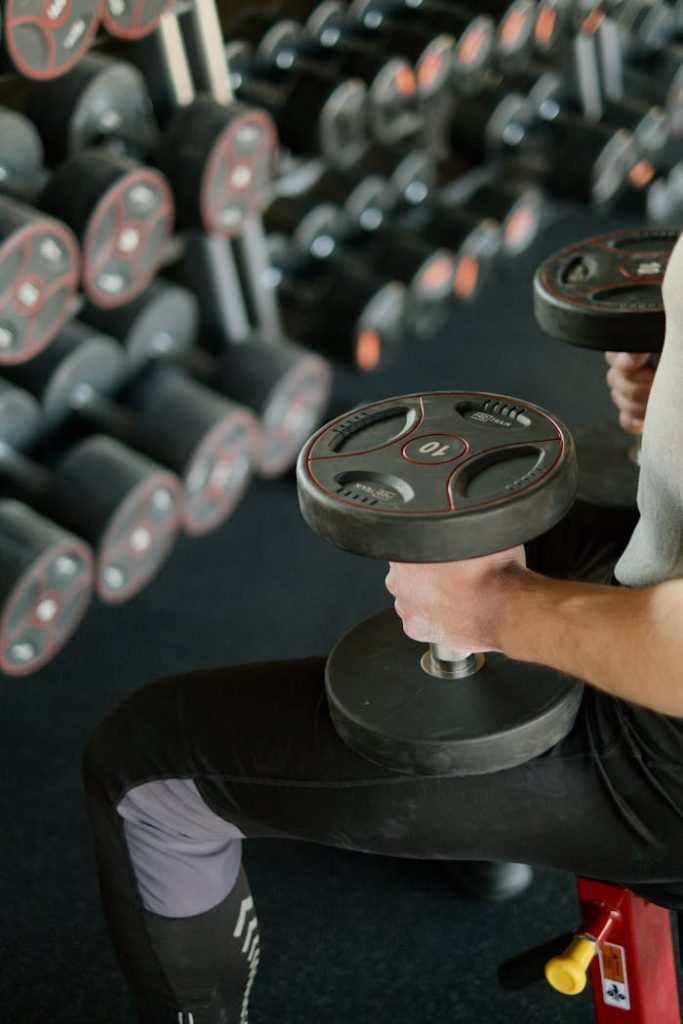 person-holding-black-dumbbells-4164761 A person lifting dumbbells while sitting on a bench in a modern gym setting.